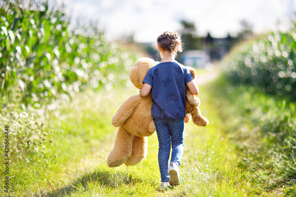 Wall mural cute little girl playing with two push toy teddies. kid holding huge bear and small bear and walking