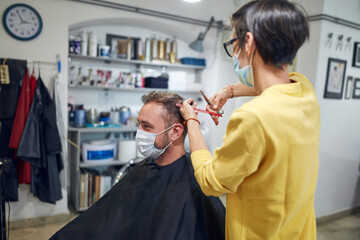 Hairdresser and customer in a salon with medical masks during virus pandemic. Working with safety mask.