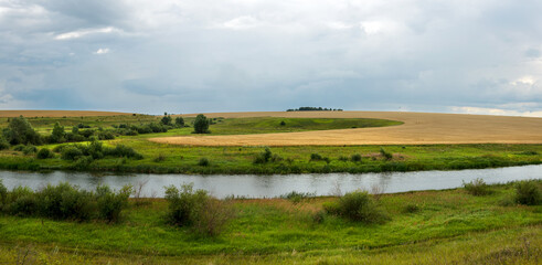 Summer cloudy landscape with dark stormy clouds over the calm river and green meadows 