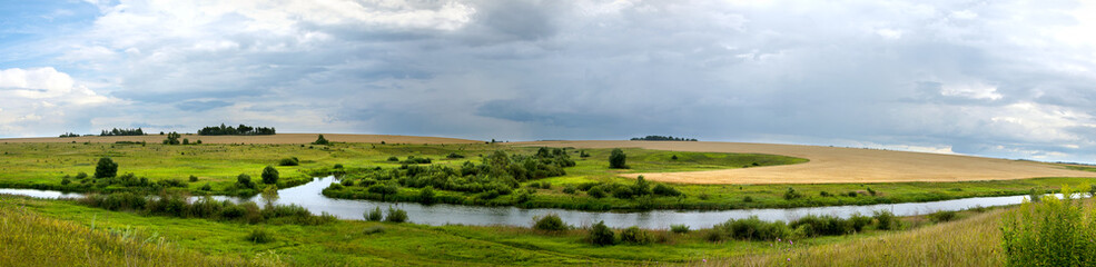 Summer cloudy landscape with dark stormy clouds over the calm river and green meadows