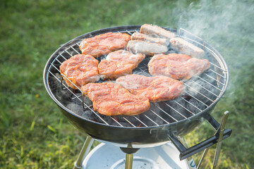 Marinierte Schweine Fleisch Nackensteaks roh grillen mit Rauch auf Holzkohle Kugelgrill im Garten an Sommer Abend