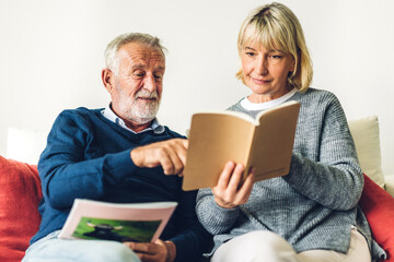 Senior couple family relax having good time reading the book together.Happy elderly husband and wife reading news and magazine while sitting on sofa at home.Retirement concept