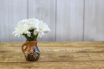 Small white fresh daisies in a brown clay vase on a light wooden background close-up