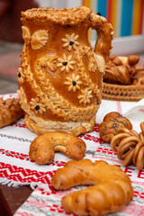 A festive loaf in the form of a jug and decorated with flowers and braids. The pie has a golden crust. A variety of pastries.