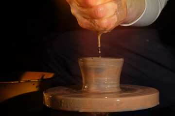 A potter makes a pot on a circle. The hands of the master moisten the clay with water. Side view