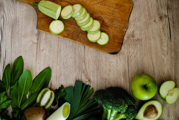 Zucchini cut into slices on a wooden board, green vegetables and fruits lie on the table.