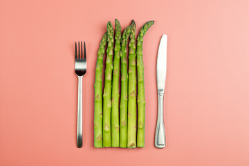 Asparagus with fork and knife on a pink background. Fresh vegetable asparagus for a healthy diet and nutrition. Vegetables and healthy food concept