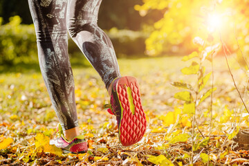 Unrecognizable woman with athletic legs on jog or run on trail in autumn forest in healthy lifestyle concept with close up on running shoes. Female athlete jogging and training at park outdoors.
