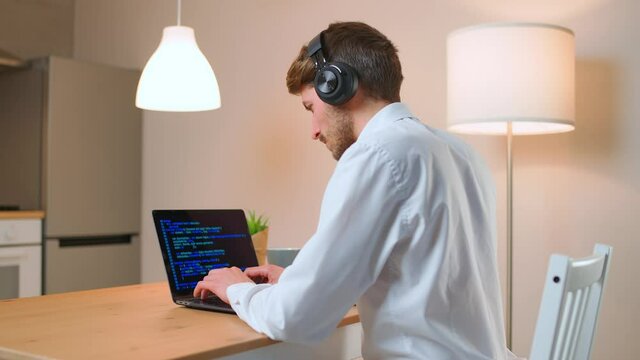 Male programmer is working on creating software, typing program code on a laptop keyboard, programmer at work, a freelancer at remote work at home.