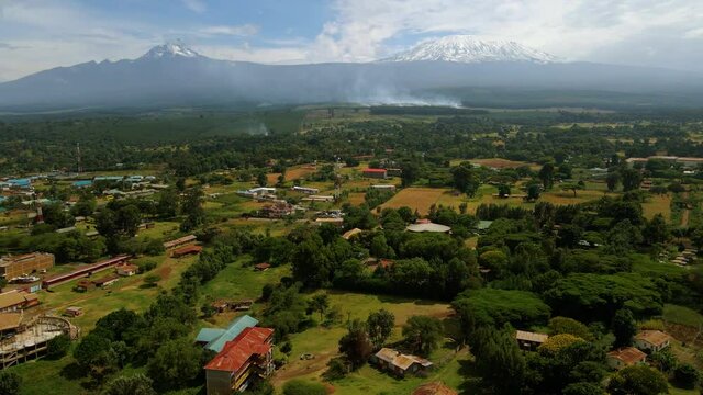 Aerial drone view rising over a houses and fields, towards burning forests, in rural Africa