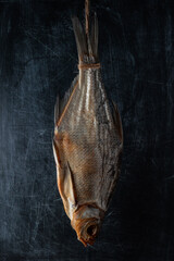 dried fish hanging from a rope against the background of a black shabby scratched wall. vertical artistic moody photo