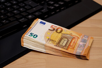 A bundle of fifty euro bills on a computer keyboard.