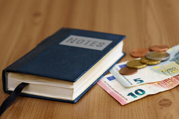 Notebook on the table next to euro banknotes and coins.