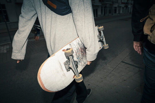 Male friends with skateboard walking on footpath at dusk