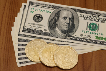 Three gold bitcoins lie on one hundred dollar bills.