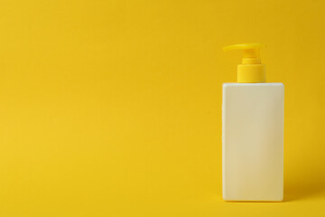 Bottle of sunscreen on yellow background, space for text