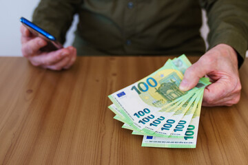 A man's hand holds out one hundred euro bills.