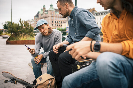 Male skaters using smart phone while sitting on footpath