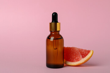 Obraz na płótnie Canvas Dropper bottle with oil and grapefruit slice on pink background