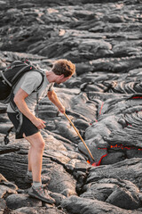 Volcanic eruption Hawaii volcano hike adventure guided tour. Man poking lava walking with backpack on black rock in Big Island, Hawaii. © Maridav