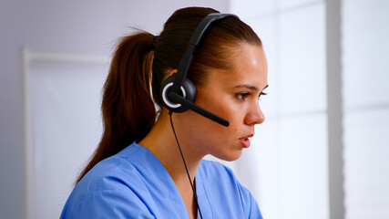 Portrait of medical receptionist answering pressing on headphone helping patient making appointment...