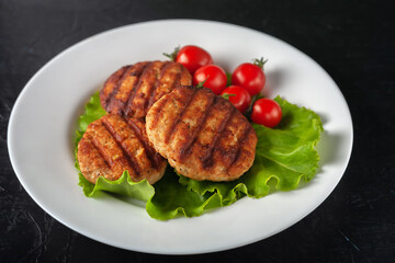 Fried cutlet with lettuce and tomatoes in a white plate on a black background