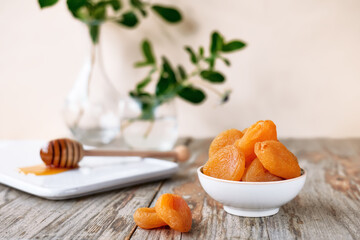 Dried apricots and honey in white plate on wooden table. Dehydrated fruits. Healthy sweets concept