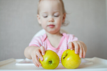 Fototapeta premium A little girl tastes, examines and plays with fresh apples with pleasure and interest. High quality photo