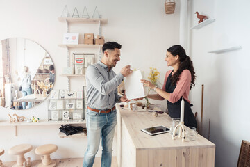Smiling male customer taking packaged product from female owner in store