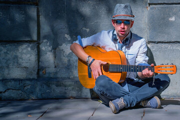 Street music art. Portrait. Male musician playing the guitar outdoors against ancient stone wall background. Horizontal image.
