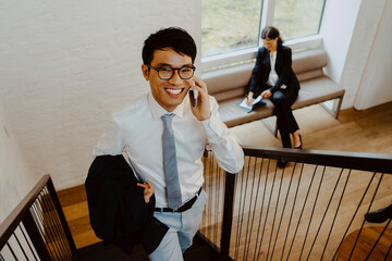 Portrait of smiling businessman talking on smart phone while climbing steps in office