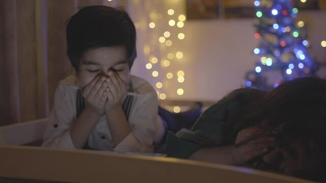 Shot of cute little dressed up Indian Asian siblings brother and sister watching cartoon movies or videos on a smartphone together with great excitement at home well-decorated home on Christmas eve