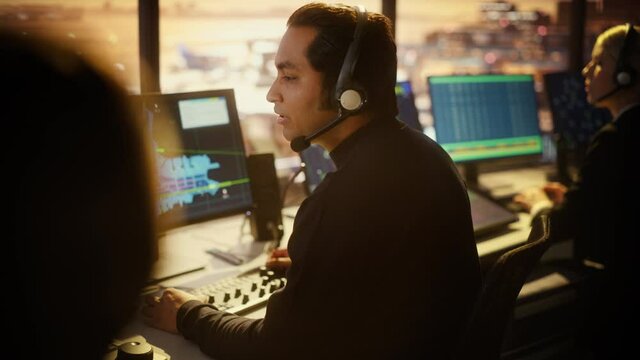 Portrait of Male Air Traffic Controller with Headset Talk on a Call in Airport Tower. Office Room is Full of Desktop Computer Displays with Navigation Screens, Airplane Flight Radar Data.