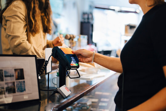 Cropped image of male customer paying through credit card to female owner at retail shop