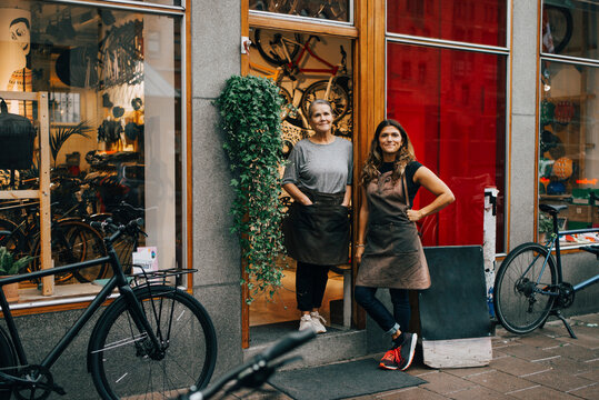 Smiling female coworkers standing at doorway of bicycle shop
