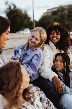 Smiling female friends talking with each other while sitting on pier