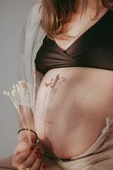 Pregnant belly close up in neutral tones and dried flowers in wabi sabi style. Pregnant woman and Future Mother