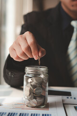 Plakat businessman saving money concept. hand holding coins putting in jug glass