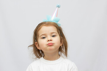 two years old blonde child party hat and tired face on white background looking seriously