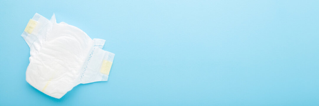 White soft new baby diaper on light blue table background. Pastel color. Closeup. Empty place for text or logo. Wide banner. Top down view.
