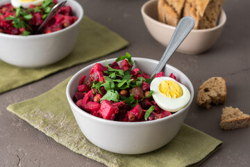 Russian salad vinaigrette in plates with boiled egg and black bread, salad of boiled potatoes and...