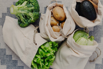 Reusable storage bags for vegetables and fruits. Storage bags with potatoes, lettuce, avocado, zucchini, broccoli. Healthy food in storage bags.