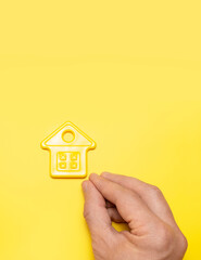 Fototapeta na wymiar House symbol in male hands on yellow background flat lay top view. Model of plastic yellow house. Concept of buying home, apartment. Renting a house, real estate. Mortgage, real estate insurance