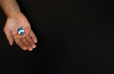 on the palm of an adult man are three tablets. On a black background. copy space
