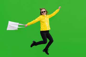 Fototapeta na wymiar Jumping woman in sunglasses with eco bag in her hand isolated on green background
