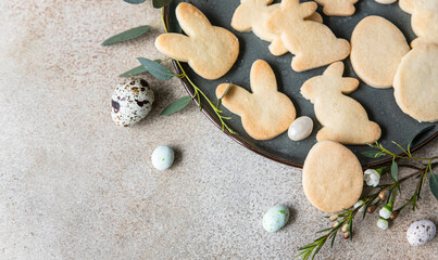 Fototapeta na wymiar Easter cookies with candies shaped eggs on a ceramic plate and floral decor and quail eggs on stone background. Homemade butter and sugar cookies. Holiday concept. Top view.