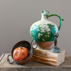 Still life with a ripe pomegranate in a copper dish, a peeling ceramic jug and a very old cast iron figurine. Retro. Vintage.