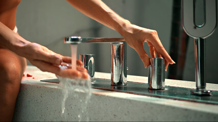 European girl sitting on a bath opens a tap with water in the bathroom with her hands