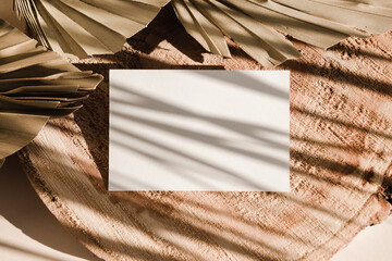 Blank card on wooden background with palm leaves shadows. Minimal concept mock up background.