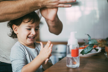 Smiling son rubbing sanitizer standing with father at home